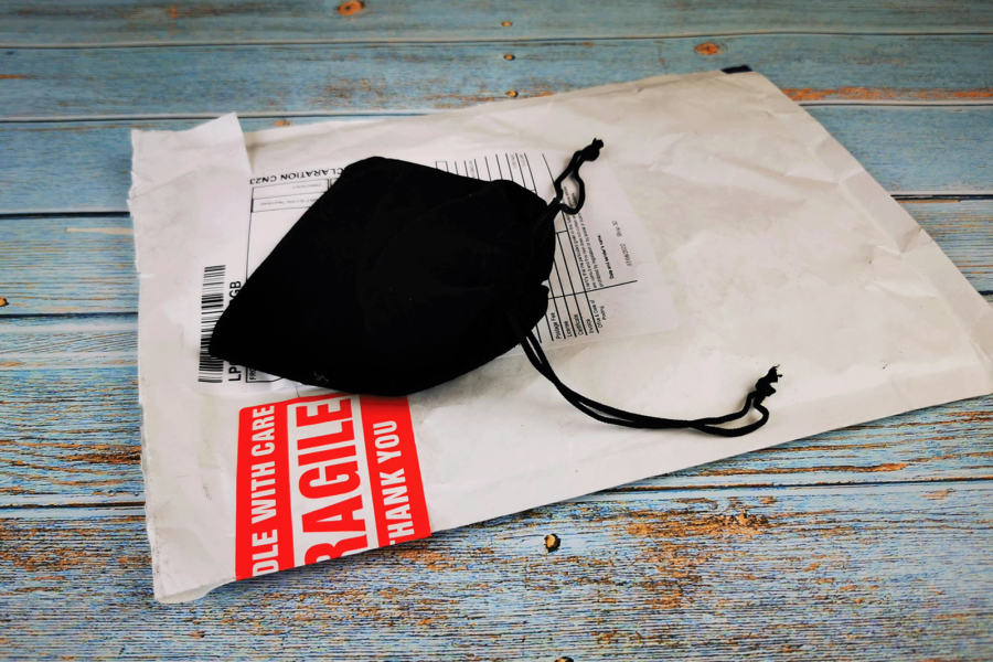 Padded envelope with a black velvet jewelry bag on top, laying on a table blue wooden table.