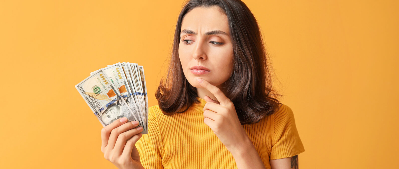 Women looking sceptically at dollar bills in front of an orange background.